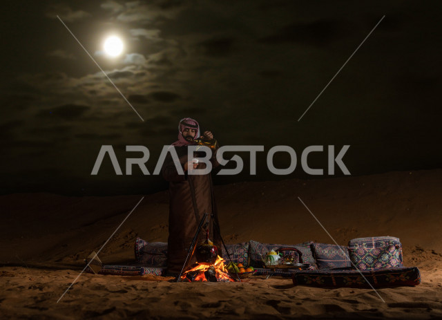 شاب سعودي يصب القهوه العربية في جلسة شعبية , أجواء مسائية في صحراء المملكة 