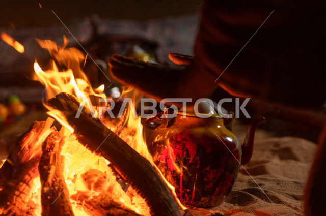 شاب سعودي يدفىء  يديه قرب شعلة الحطب , موسم الشتاء في صحاري المملكة العربية السعودية , تخييم رجل سعودي في الصحراء 