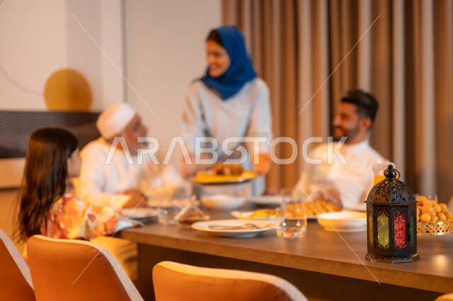 تبادل الأحاديث بين أفراد الأسرة، أجواء عائلية دينية رمضانية سعيدة، عائلة عربية خليجية سعودية مجتمعة حول مائدة الطعام، سفرة مليئة بأصناف من المأكولات الشرقية الشهية، أداء فريضة الصيام في شهر رمضان المبارك، زينة المناسبات الإسلامية