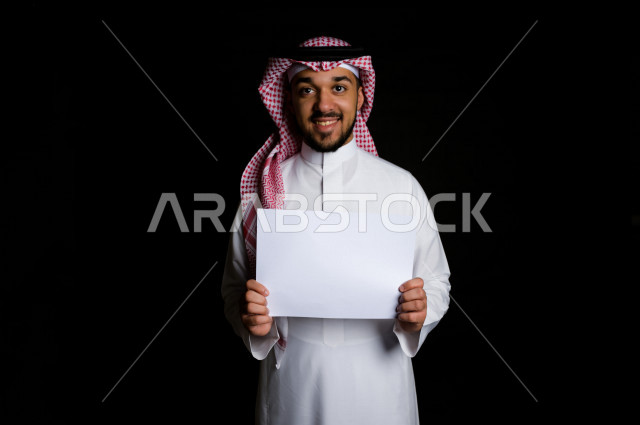 بورتريه لرجل سعودي خليجي سعيد بإيماءات الوجه المختلفة ، تعابير وجه و يدين مختلفة , يمسك بيده لوحة بيضاء ، خلفية سوداء