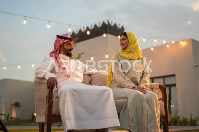 نظرات مليئة بالحب, مفهوم الرابطة الزوجية والألفة بين الزوجين, زوجان عربيان خليجيان سعوديان يجلسان في حديقة المنزل, شقق وفلل سكنية راقية في المملكة العربية السعودية, الاستمتاع بالنقاشات والحوارات العائلية في الهواء الطلق