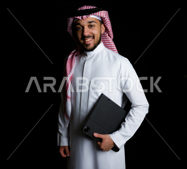 شاب خليجي عربي سعودي يمسك بيده جهاز لوحي , خلفية سوداء 
