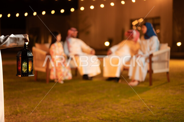 فوانيس معدنية مضيئة وديكورات وزينة المناسبات والأعياد الاسلامية الدينية، أسرة عربية خليجية سعودية تقضي وقت ممتع في جلسة خارجية في احدى الشاليهات، أجواء عائلية سعيدة في شهر رمضان المبارك