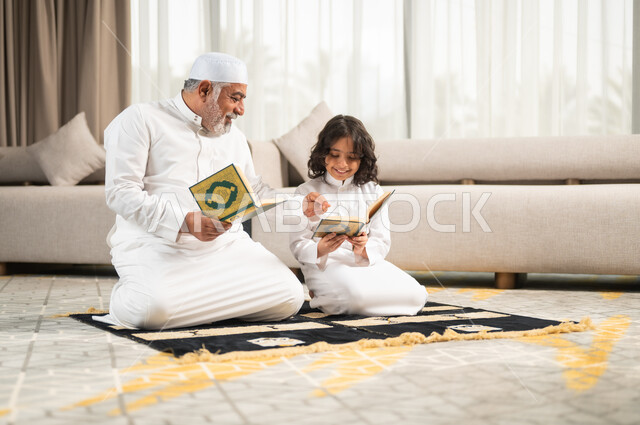 الجلسات الروحانية في شهر رمضان المبارك، زرع الفطرة السليمة في الاولاد، قراءة وتلاوة القرآن الكريم، رجل كبير عربي خليجي سعودي يرتدي الطاقية البيضاء والثوب التقليدي يجلس على سجادة الصلاة بجانب حفيده، اداء الفرائض الدينية، الاجتهاد بالطاعة والتقرب الى الله