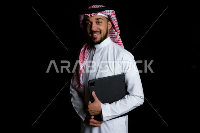 شاب خليجي عربي سعودي يمسك بيده جهاز لوحي , خلفية سوداء 