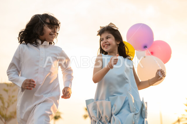 الاستمتاع مع الأخوات بإيماءات البشاشة والسرور, أعياد ومناسبات اسلامية سعيدة, فرحة وبهجة الأطفال بقدوم العيد, ولد وفتاة عربيان خليجيان سعوديان يقومان بالركض في إحدى الشاليهات والمنتجعات السياحية,لحظات ممتعه مليئة بتعابير الفرح