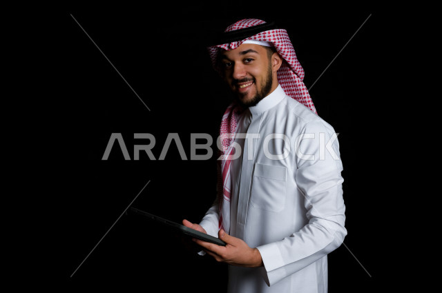 شاب خليجي عربي سعودي يمسك بيده جهاز لوحي , خلفية سوداء 