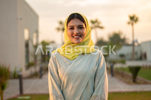 مفهوم النعومة والشياكة وإبراز الجمال الخليجي, صورة مقربة لشابة عربية خليجية سعودية ترتدي الحجاب والعباءة تنظر إلى الكاميرا بإيماءات السرور والبشاشة, الأناقة والاهتمام بالمظهر الخارجي, قضاء الوقت الممتع والاستمتاع في الهواء الطلق