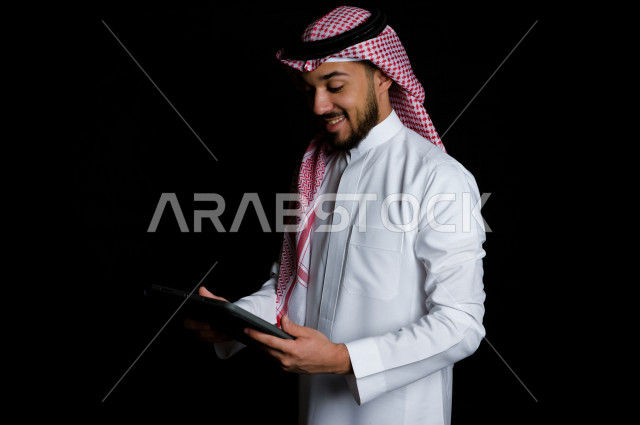 شاب خليجي عربي سعودي يمسك بيده جهاز لوحي , خلفية سوداء 
