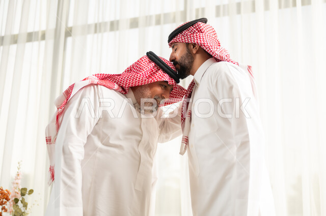 تعابير التقدير واحترام كبار السن, التمسك بالعادات والتقاليد, مفهوم الترابط الأسري وصلة الرحم, أجواء عائلية راقية في الأعياد والمناسبات السعيدة, شاب عربي خليجي سعودي يرتدي الزي التقليدي يقوم بتقبيل والده, ايماءات إلقاء التحية والسلام
