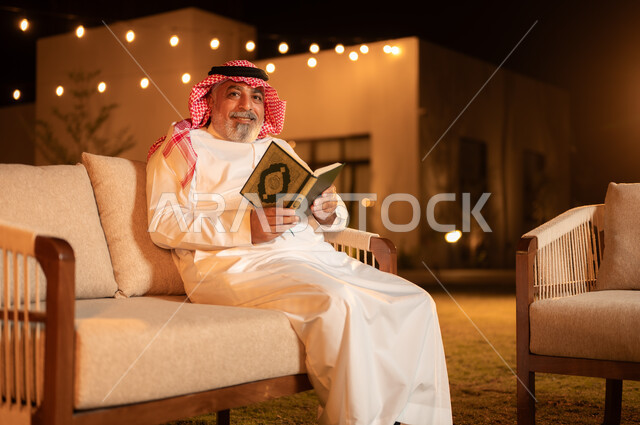 الاجتهاد في العبادة واداء الفرائض الدينية، تلاوة وحفظ المصحف الشريف، رجل كبير بالسن عربي سعودي خليجي مسلم يرتدي الشماغ والثوب التقليدي يقوم بقراءة القرآن الكريم، الجلوس في الهواء الطلق في حديقة احدى الشاليهات الفاخرة، التقرب الى الله في شهر رمضان المبارك