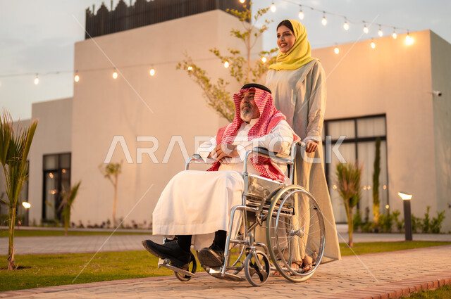 شعور ذوي الهمم بالراحه والطمأنينه في بيئتهم, رحلات عائلية سعيدة في إحدى الشاليهات والمنتجعات السياحية الراقية, دعم المجتمع السعودي لذوي الاحتياجات الخاصه, إمرأة عربية خليجية سعودية ترتدي العباءة والحجاب تقوم بمساعدة والدها المقعد على الحركة