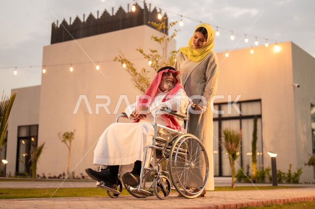شعور ذوي الهمم بالراحه والطمأنينه في بيئتهم, رحلات عائلية سعيدة في إحدى الشاليهات والمنتجعات السياحية الراقية, دعم المجتمع السعودي لذوي الاحتياجات الخاصه, إمرأة عربية خليجية سعودية ترتدي العباءة والحجاب تقوم بمساعدة والدها المقعد على الحركة
