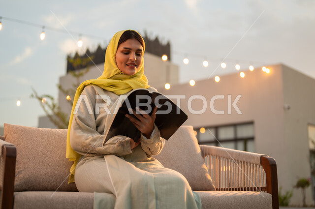 مفهوم الثقافة والاطلاع والتعلم الذاتي, إمرأة عربية خليجية سعودية ترتدي العباءة والحجاب الأصفر تقوم بالقراءة والمطالعة في الهواء الطلق, الشغف بممارسة الهوايات المفيدة, الأنشطة الترفيهية الثقافية