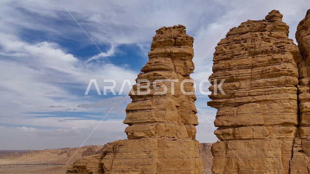 التكوينات الصخرية الطبيعيه في المناطق الصحراوية, تشكيل صخري من الحجر الرملي الطبيعي في سلسلة جبال طويق، معالم وأماكن سياحيه مشهورة في صحاري المملكة العربية السعودية, خلفية السماء المليئة بالغيوم البيضاء