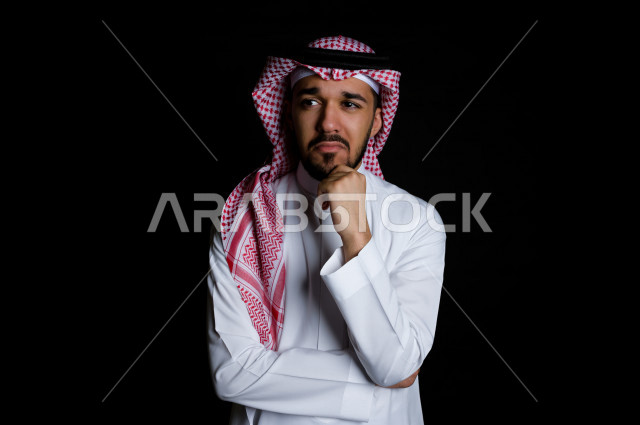 بورتريه لرجل سعودي خليجي سعيد بإيماءات الوجه المختلفة ، تفكير باليد على الذقن ، خلفية سوداء