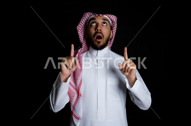 بورتريه لرجل سعودي خليجي عربي ينظر إلى الأعلى , برفع إصبعين السبابة  , خلفية سوداء 