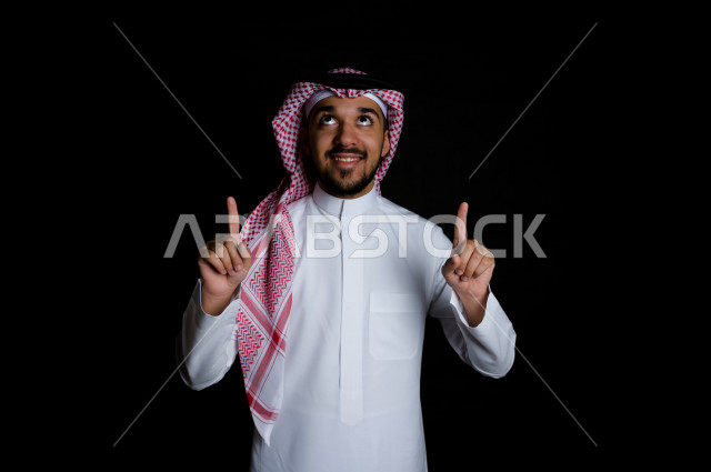 بورتريه لرجل سعودي خليجي عربي ينظر إلى الأعلى , برفع إصبعين السبابة  , خلفية سوداء 