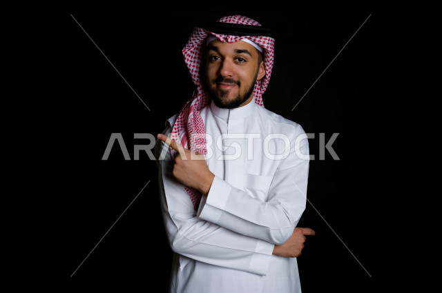 بورتريه لرجل سعودي خليجي سعيد بإيماءات الوجه المختلفة ، تعابير وجه و يدين مختلفة ،رفع اصبع السبابة مع ضم يده ,  خلفية سوداء