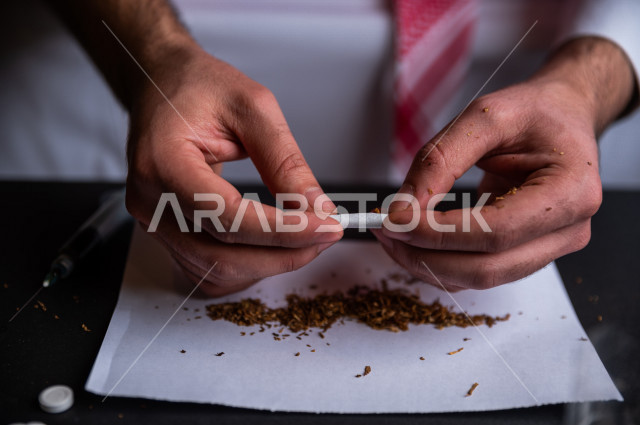 شاب عربي سعودي مدخن ، يقوم بلف السجائر بيديه داخل ورق مخصص للتبغ، الادمان على التبغ ، ادمان السجائر ، تعاطي مواد ضارة و سامة ، عادات سلوكية ضارة ، لا للتدخين