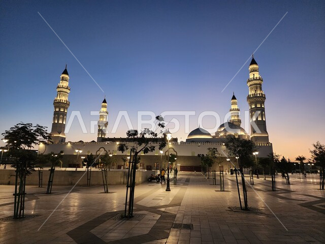 الساحة الخارجية لمسجد قباء في المدينة المنورة وقت الغروب، دعوة المسلمين لآداء الصلاة والتقرب إلى الله تعالى، معالم وأماكن دينية مقدسة في المملكة العربية السعودية، المآذن و القبب المضيئة، الفن الهندسي المعماري والديكورات الاسلامية على الطراز الحديث