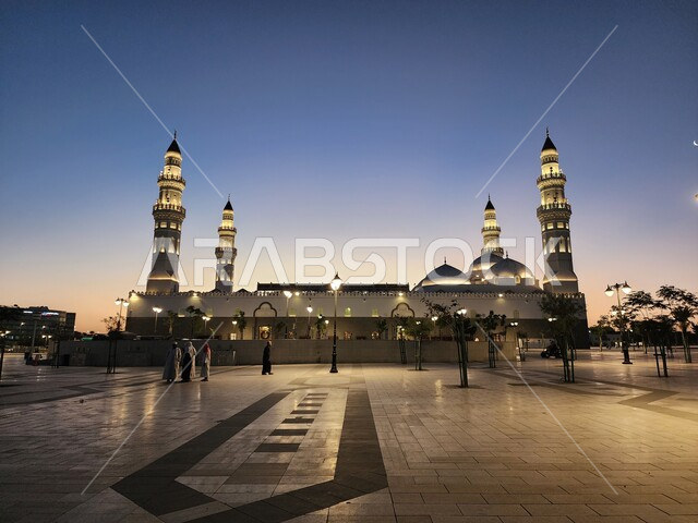 الساحة الخارجية لمسجد قباء في المدينة المنورة وقت الغروب، دعوة المسلمين لآداء الصلاة والتقرب إلى الله تعالى، معالم وأماكن دينية مقدسة في المملكة العربية السعودية، المآذن و القبب المضيئة، الفن الهندسي المعماري والديكورات الاسلامية على الطراز الحديث
