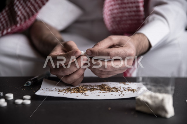 شاب عربي سعودي مدخن ، يقوم بلف السجائر بيديه داخل ورق مخصص للتبغ، الادمان على التبغ ، ادمان السجائر ، تعاطي مواد ضارة و سامة ، عادات سلوكية ضارة ، لا للتدخين