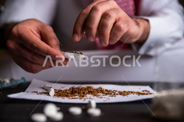 شاب عربي سعودي مدخن ، يقوم بلف السجائر بيديه داخل ورق مخصص للتبغ، الادمان على التبغ ، ادمان السجائر ، تعاطي مواد ضارة و سامة ، عادات سلوكية ضارة ، لا للتدخين