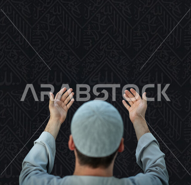 التضرع و طلب العون والحمد والشكر، العباده والتقرب الى الله، صورة مقربة من الخلف لرجل عربي خليجي سعودي مسلم يرتدي ثوب تقليدي وقبعة رمادية يرفع يديه للدعاء، خلفية اسلامية سوداء