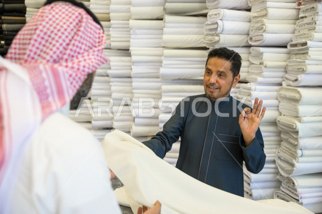 شاب سعودي خليجي يعمل في مهنة الخياطة ، يعرض للزبون اجود انواع الأقنشة لتفصيل الثوب السعودي ، محل خياطة و تفصيل الملابس الرجالي في السعودية ، مهارة الخياطة واتقان تفصيل الملابس الشبابية
