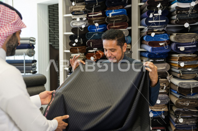 شاب سعودي خليجي يعمل في مهنة الخياطة ، يعرض للزبون اجود انواع الأقنشة لتفصيل الثوب السعودي ، محل خياطة و تفصيل الملابس الرجالي في السعودية ، مهارة الخياطة واتقان تفصيل الملابس الشبابية
