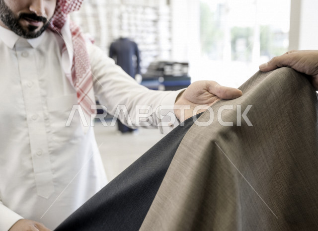 شاب سعودي خليجي يعمل في مهنة الخياطة ، يعرض للزبون اجود انواع الأقنشة لتفصيل الثوب السعودي ، محل خياطة و تفصيل الملابس الرجالي في السعودية ، مهارة الخياطة واتقان تفصيل الملابس الشبابية