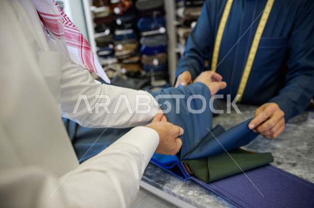 شاب سعودي خليجي يعمل في مهنة الخياطة ، يعرض للزبون اجود انواع الأقنشة لتفصيل الثوب السعودي ، محل خياطة و تفصيل الملابس الرجالي في السعودية ، مهارة الخياطة واتقان تفصيل الملابس الشبابية