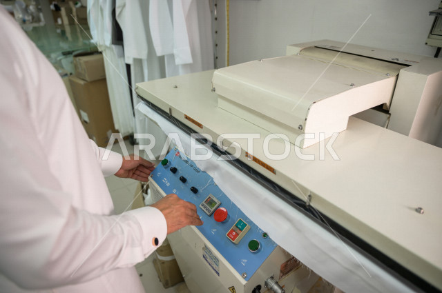 شاب سعودي خليجي يعمل في مهنة الخياطة ، يستخدم الأدوات المناسبة لتفصيل جلابية خاصة لاحدى الزبائن ، محل خياطة و تفصيل الملابس الرجالي في السعودية ، مهارة الخياطة واتقان تفصيل الملابس الشبابية