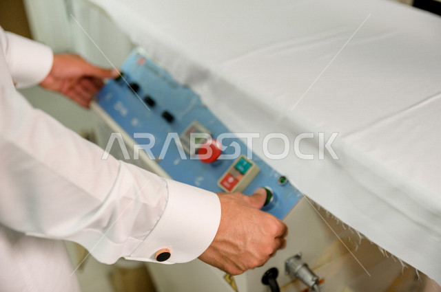 شاب سعودي خليجي يعمل في مهنة الخياطة ، يستخدم الأدوات المناسبة لتفصيل جلابية خاصة لاحدى الزبائن ، محل خياطة و تفصيل الملابس الرجالي في السعودية ، مهارة الخياطة واتقان تفصيل الملابس الشبابية