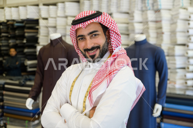 A young Saudi Gulf man working in the profession of sewing, he takes measurements of the customer's body in terms of length, width and waist using metric tape, a shop for sewing and tailoring men's clothes in Saudi Arabia, sewing skill and mastering the d