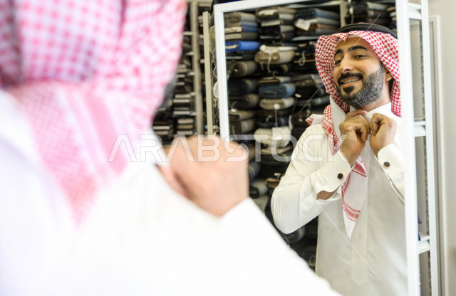 A young Saudi Gulf man inside a shop specializing in detailing men's clothes, measuring his dishdasha, a men's tailoring and tailoring shop in Saudi Arabia, sewing skill and mastering the tailoring of youthful clothes