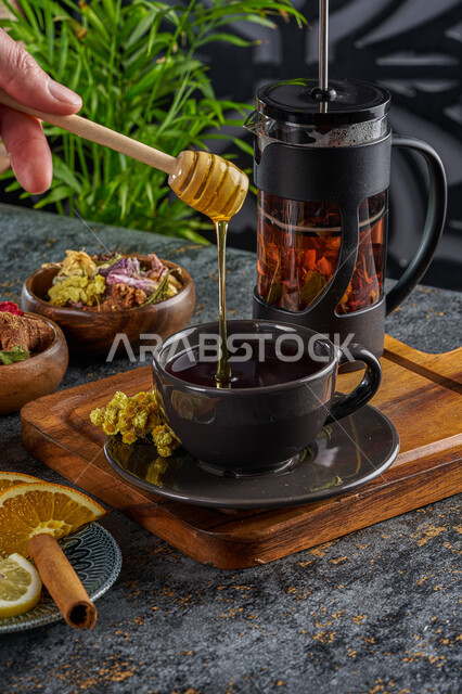 Adding honey to drinks, healthy natural sugars, a local Saudi national product, a pot of herbal tea with a glass cup, a meal with a high nutritional value, using natural plants and cinnamon as an alternative to medicine.