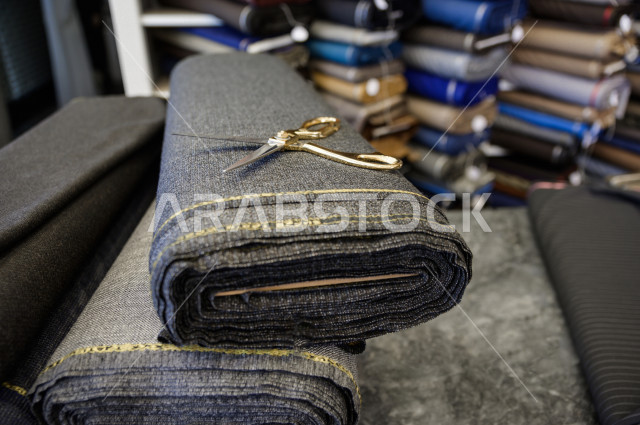 شاب سعودي خليجي يعمل في مهنة الخياطة ، يعرض للزبون اجود انواع الأقنشة لتفصيل الثوب السعودي ، محل خياطة و تفصيل الملابس الرجالي في السعودية ، مهارة الخياطة واتقان تفصيل الملابس الشبابية