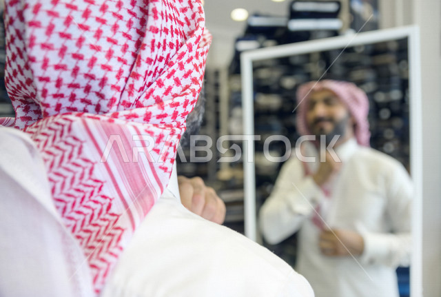 شاب سعودي خليجي داخل محل مختص بتفصيل الملابس الرجالية ، يقوم بقياس الدشداشة الخاص به، محل خياطة و تفصيل الملابس الرجالي في السعودية ، مهارة الخياطة واتقان تفصيل الملابس الشبابية