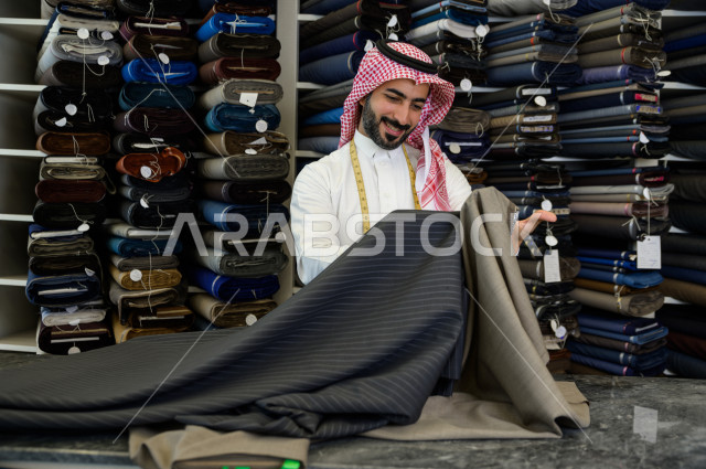شاب سعودي خليجي يعمل في مهنة الخياطة ، اختيار اجود انواع الأقنشة لتفصيل الثوب السعودي ، محل خياطة و تفصيل الملابس الرجالي في السعودية ، مهارة الخياطة واتقان تفصيل الملابس الشبابية