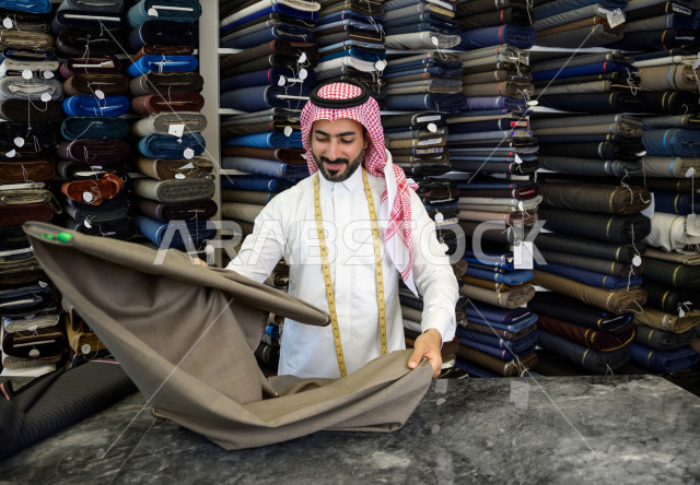 شاب سعودي خليجي يعمل في مهنة الخياطة ، اختيار اجود انواع الأقنشة لتفصيل الثوب السعودي ، محل خياطة و تفصيل الملابس الرجالي في السعودية ، مهارة الخياطة واتقان تفصيل الملابس الشبابية