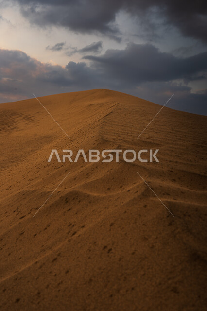 View of the sky filled with dark clouds, landscapes in the desert environment in the Kingdom of Saudi Arabia, soft golden sand formations, places for activities and safari trips in the desert, hills and sand dunes