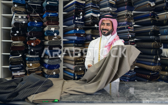 شاب سعودي خليجي يعمل في مهنة الخياطة ، اختيار اجود انواع الأقنشة لتفصيل الثوب السعودي ، محل خياطة و تفصيل الملابس الرجالي في السعودية ، مهارة الخياطة واتقان تفصيل الملابس الشبابية