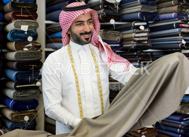 شاب سعودي خليجي يعمل في مهنة الخياطة ، اختيار اجود انواع الأقنشة لتفصيل الثوب السعودي ، محل خياطة و تفصيل الملابس الرجالي في السعودية ، مهارة الخياطة واتقان تفصيل الملابس الشبابية