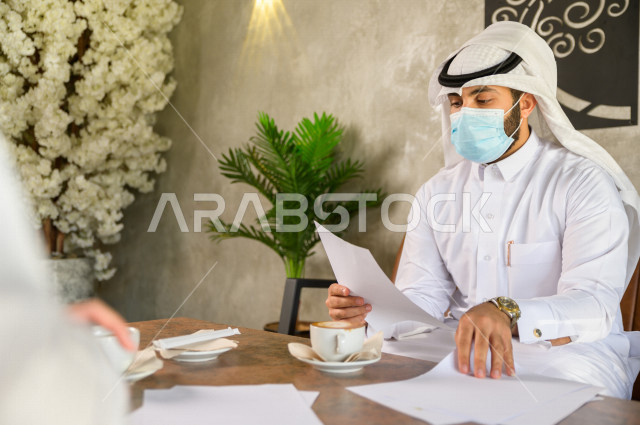 رجلان سعوديان في مقابة عمل يرتديان الكمامة داخل المقهى , بيئة عمل صحية , الحماية من كورونا  