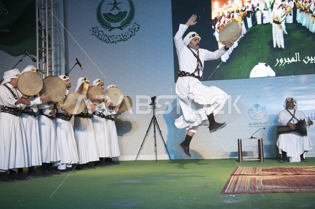 مجموعة رجال عرب خليجييون سعودييون يرتدون الثوب الحويسي التقليدي يؤدون رقصة المزمار والمجرور، رقصات الفن الشعبي في منطقة الحجاز، الشعر والغناء والرقص، المناسبات والأعياد والمهرجانات الثقافية والتراثية، الفلكلورات والأهازيج الشعبية