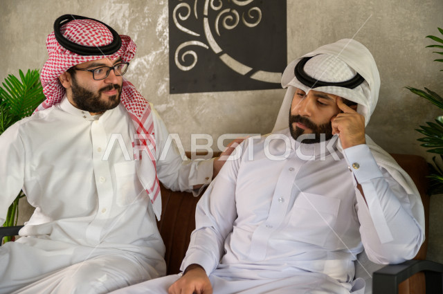 شابان عربيان سعوديان يجلسان في المقهى , احدهم يشعر بالحزن والاخر يقوم بمواساة صديقه , شاب عربي حزين , 