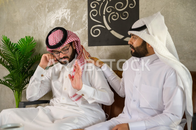 Saudi friends sitting in a cafe , a sad youth man with his friend , saudi man consoles his friend 