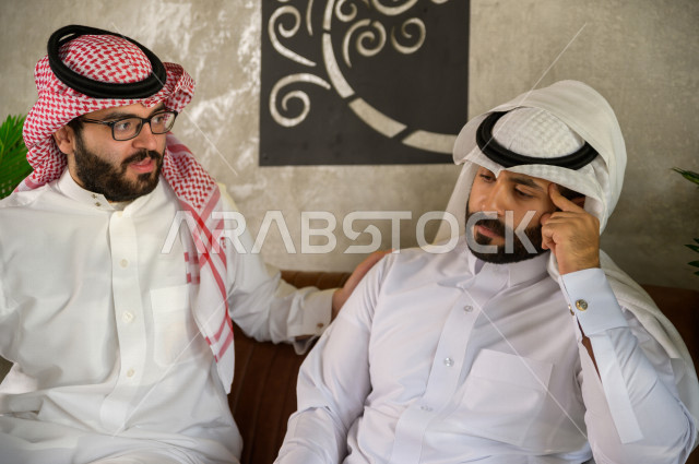 شابان عربيان سعوديان يجلسان في المقهى , احدهم يشعر بالحزن والاخر يقوم بمواساة صديقه , شاب عربي حزين , 